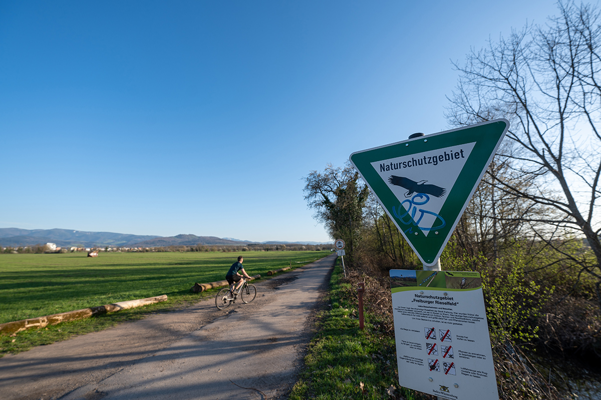 Schild "Naturschutzgebiet" vor einer Wiese mit Weg