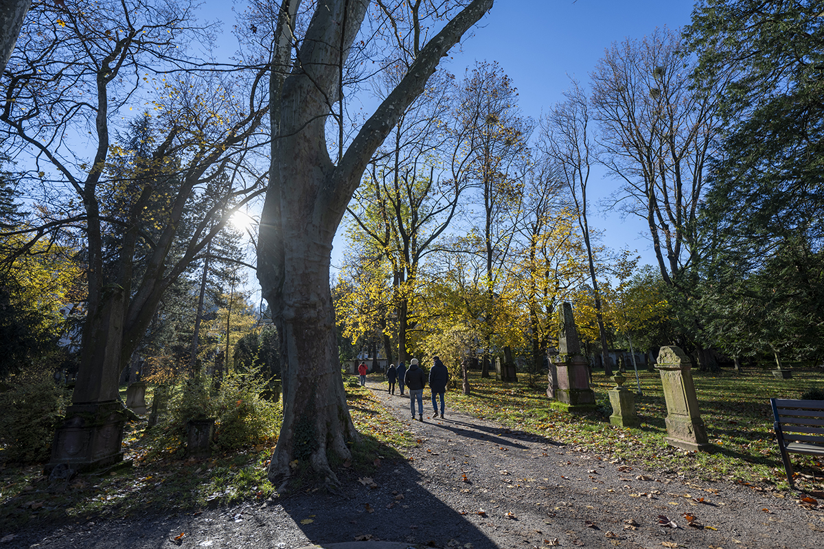 Menschen, die auf dem Friedhof spazieren gehen; Gräber und Bäume