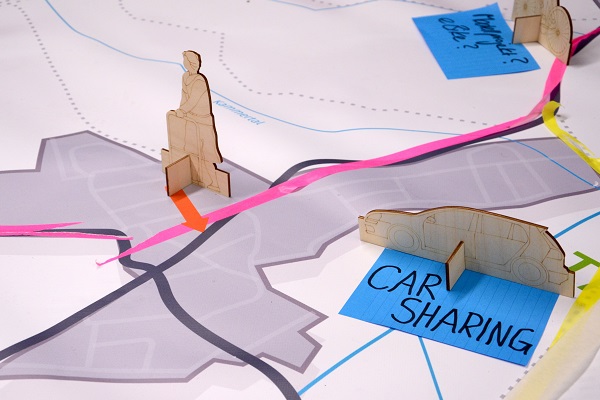 Planzeichnung mit Pappfiguren von Menschen und Autos, Schrift "Car-Sharing"