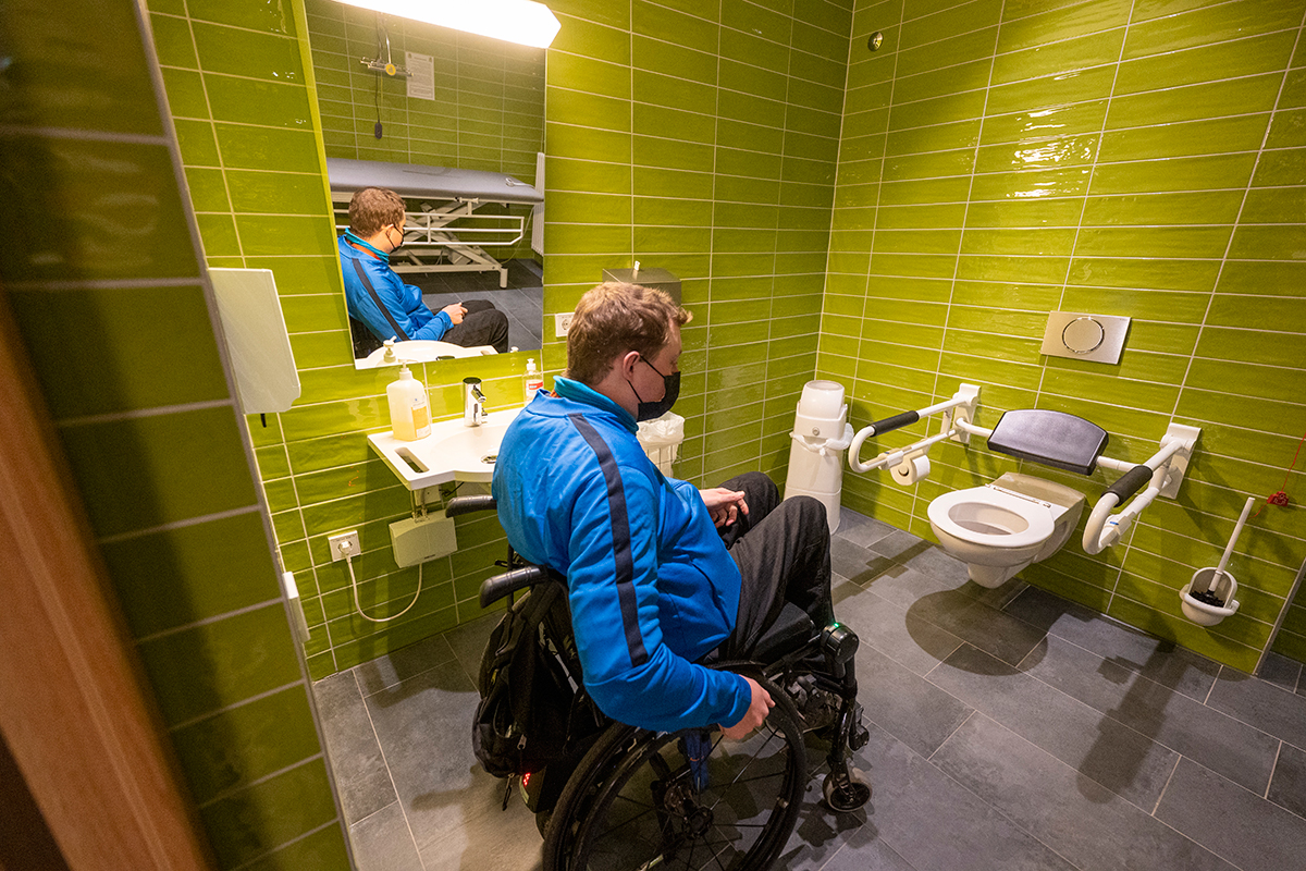 Ein Mann im Rollstuhl in einer barrierefreien Toilette mit grünen Kacheln